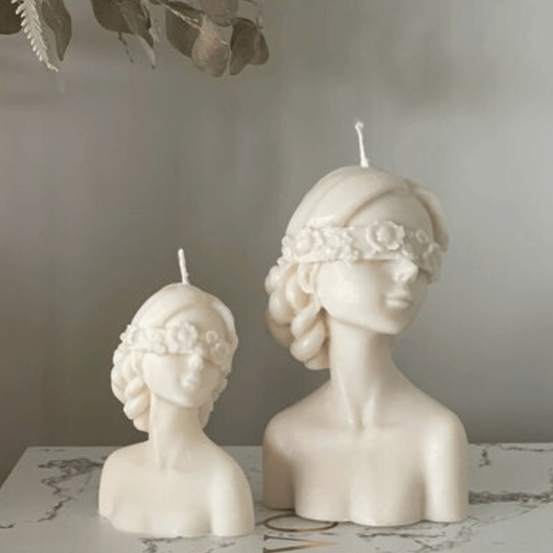 two floral blindfolded female torso candles in different sizes in white on a marble bench with a grey background