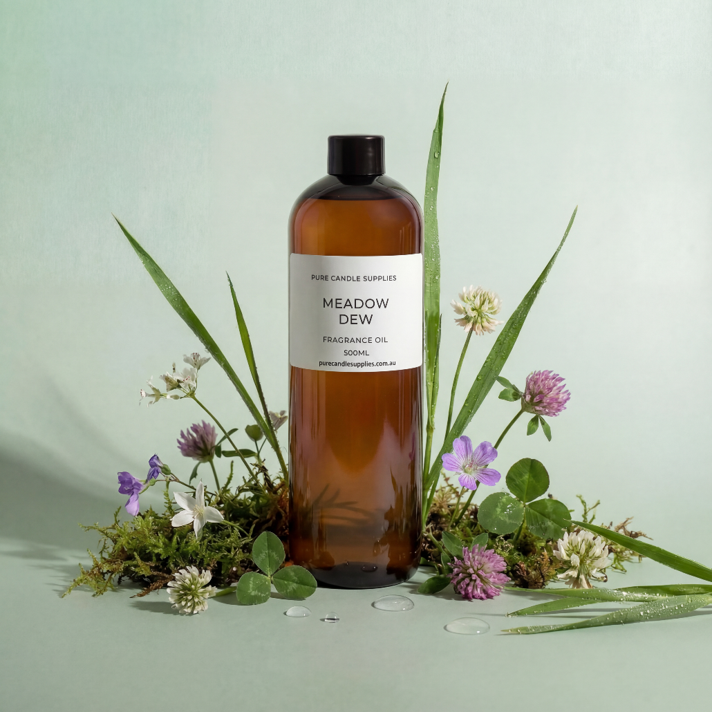 Bottle of 'Meadow Dew' fragrance oil surrounded by greenery and flowers on a light green background