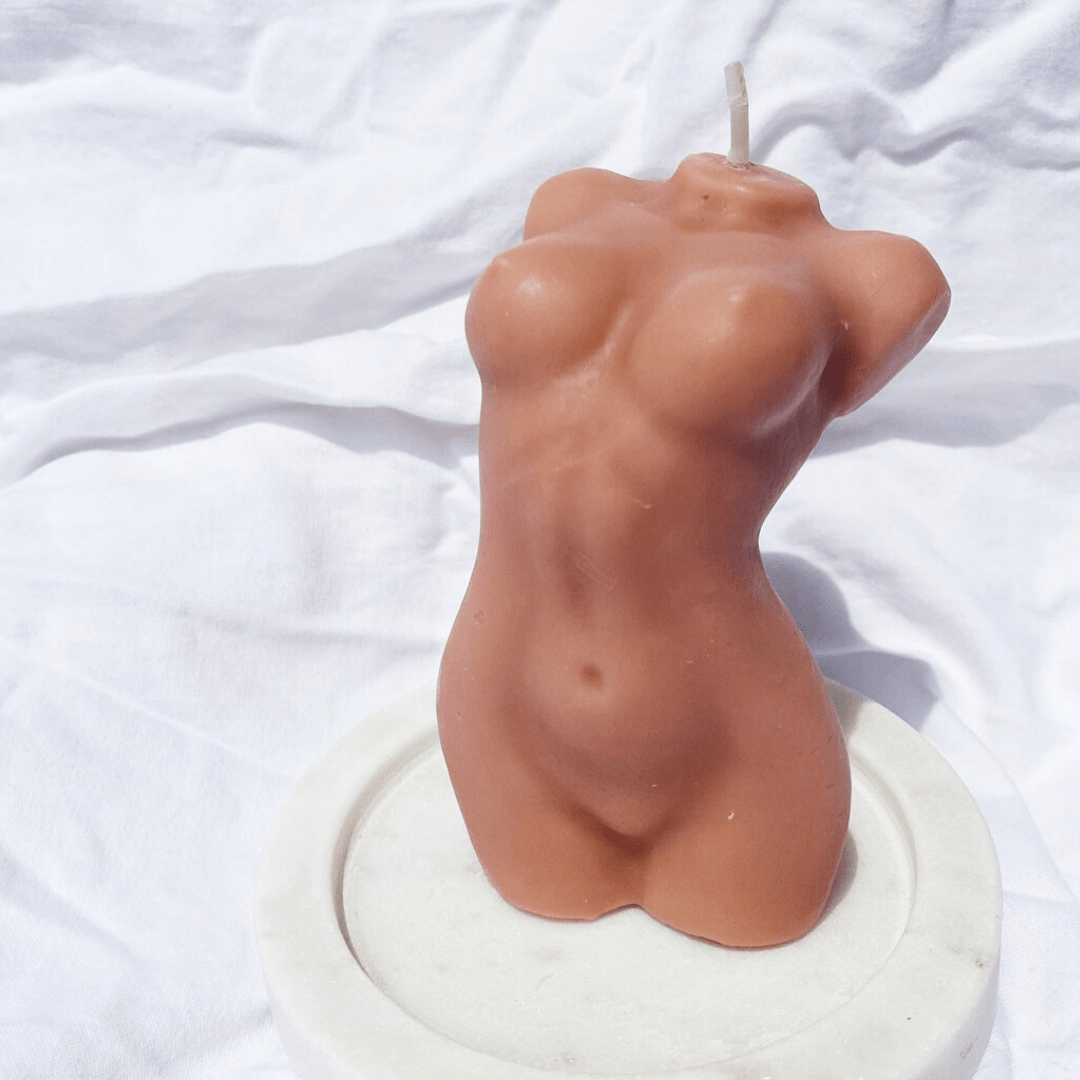 brown female body candle on white stand with white linen background