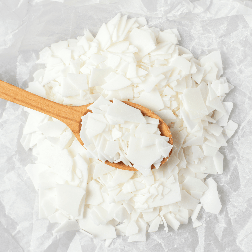 flaked soy wax resting on spoon with flaked wax and tissue paper in background