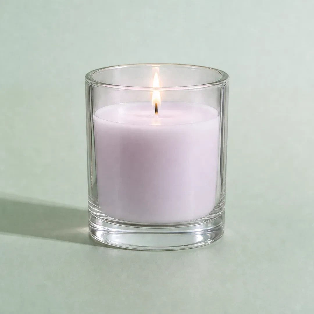 Pure Candle Supplies Melbourne lavender candle in a clear glass container with a lit wick on a soft green background