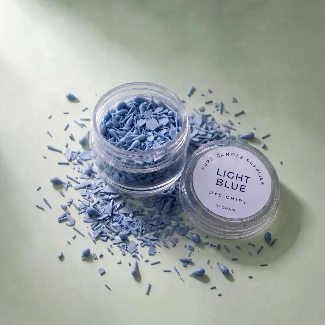 Pure Candle Supplies Melbourne light blue candle dye chips in a clear jar with scattered pieces on a green surface.