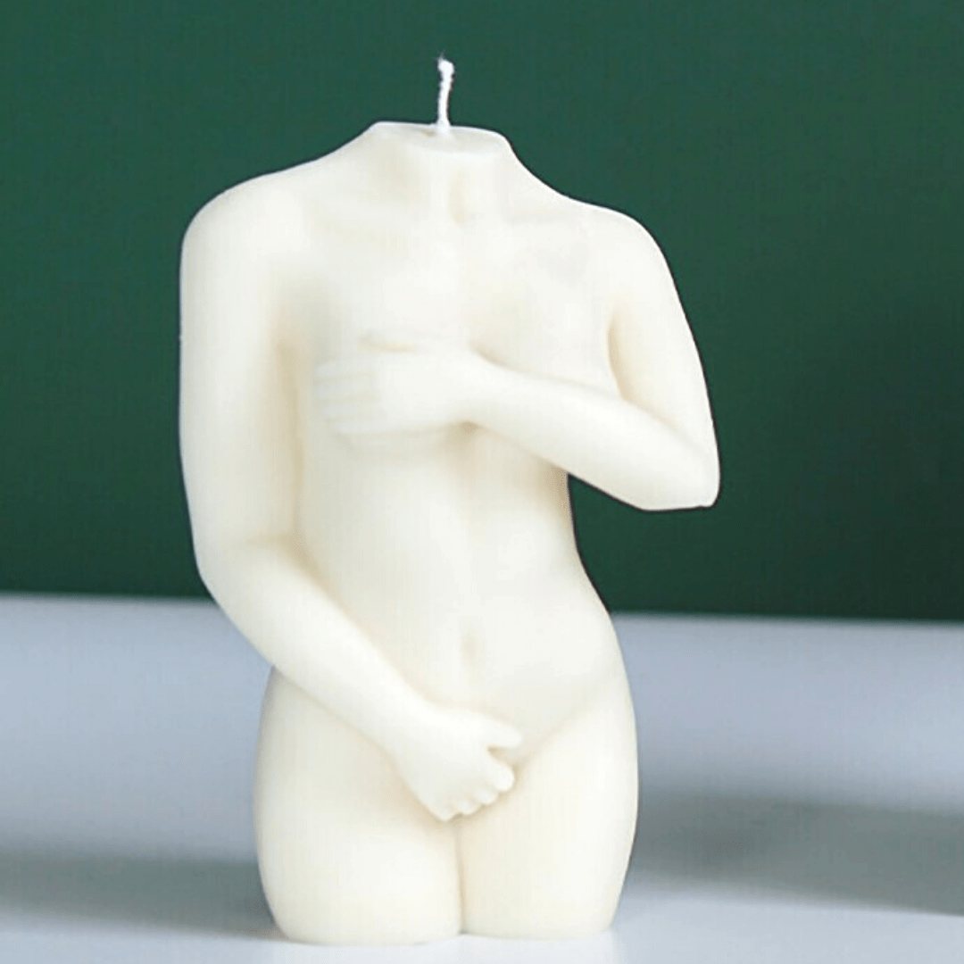 female body candle with arms wrapped around body in white wax on white table against green wall