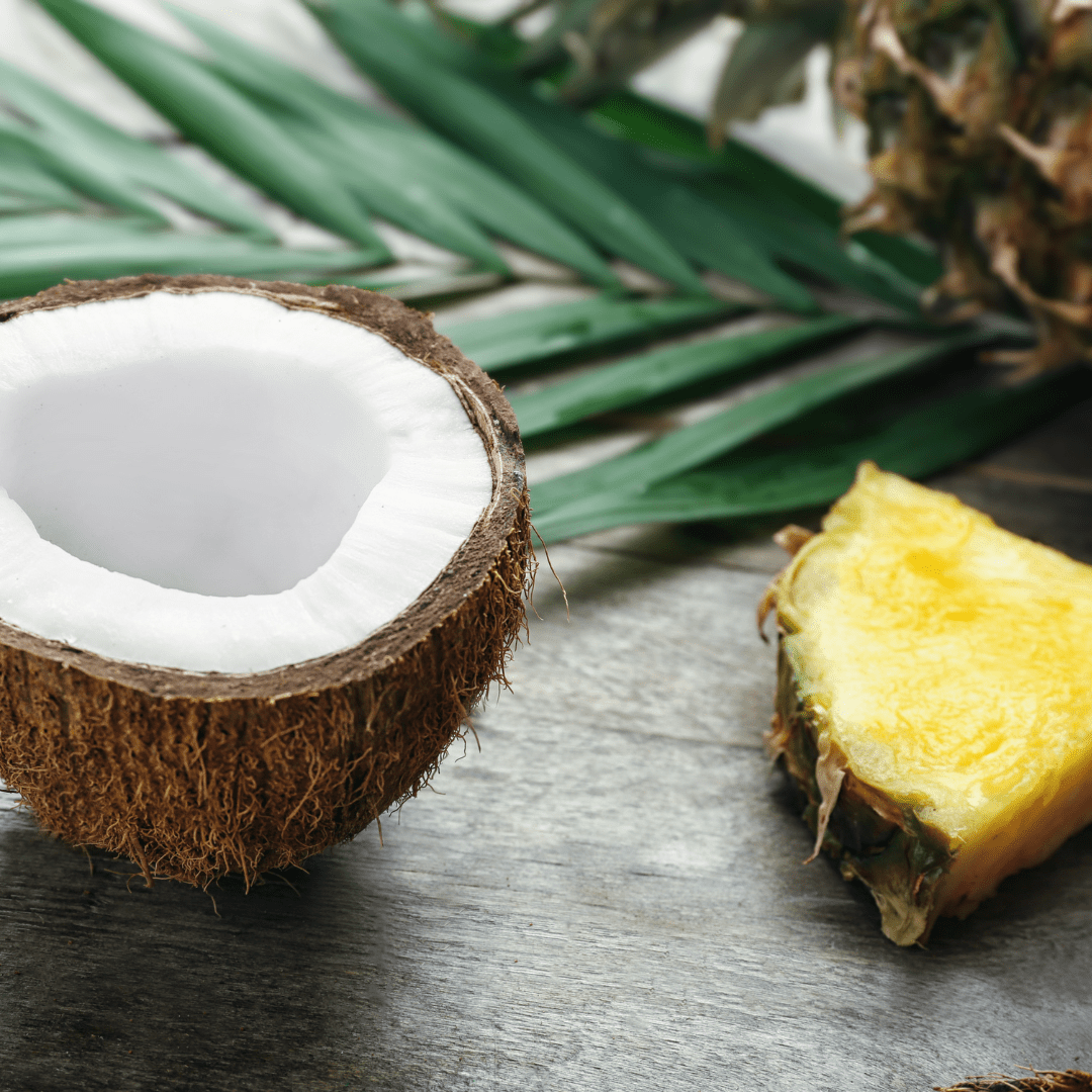 Open coconut with fresh slice of pineapple and palm leaf in background