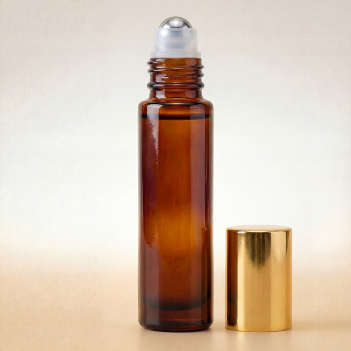 Amber glass roller bottle with silver cap and gold lid on a beige background