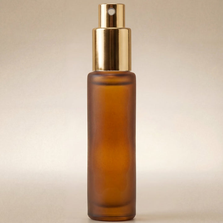 Amber glass spray bottle with gold cap on a beige background