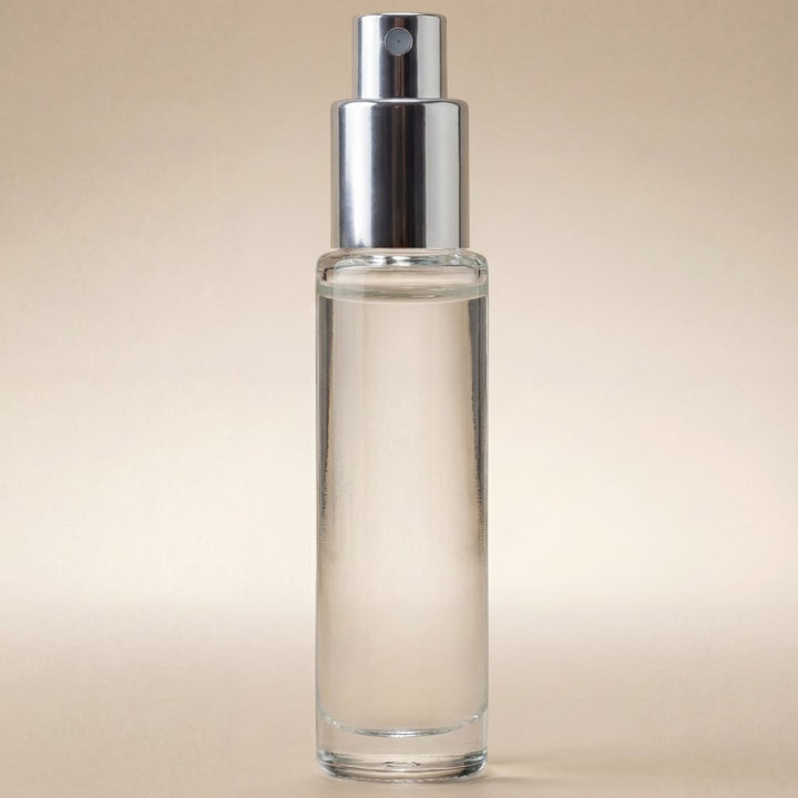 Clear glass spray bottle with silver nozzle on a beige background