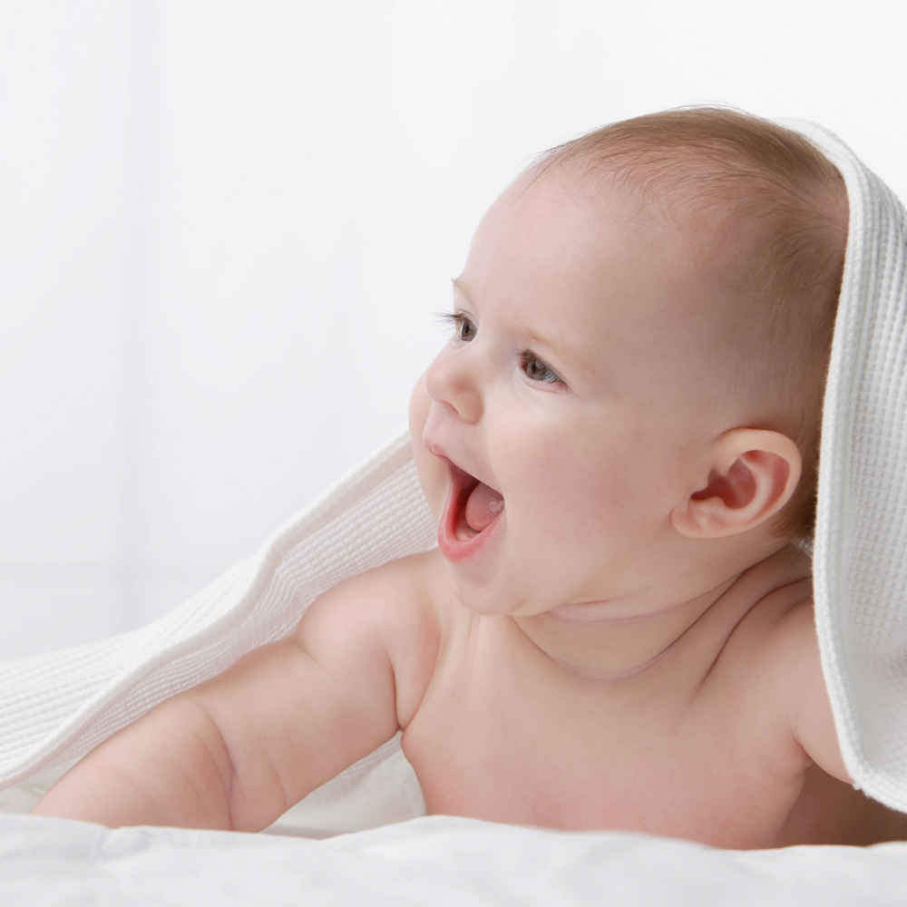 a baby on their tummy with thwir head poking out through a towel