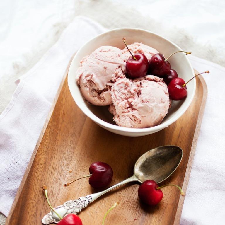 bowl of cherry sorbet with cherries surrounding on wooden board