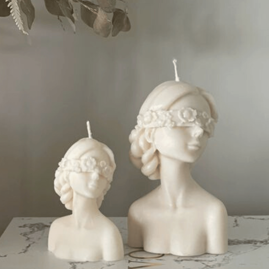 two floral blindfolded female torso candles in different sizes in white on a marble bench with a grey background 