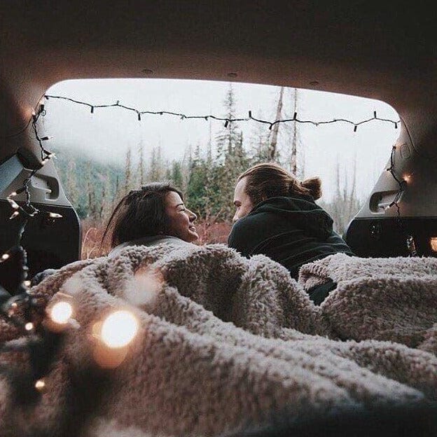 Couple in back of car under warm cashmere blanket looking towards the forest