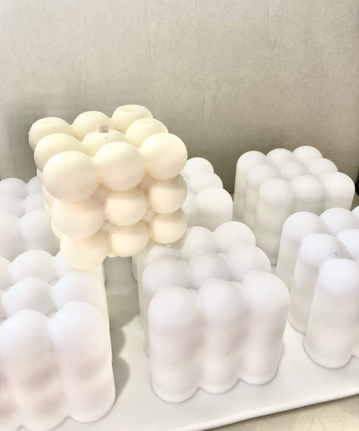 cube bubble candle in cream on top of white 6 cavity bubble cube mould with grey background