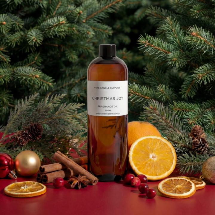 Bottle of 'Christmas Joy' fragrance oil with festive elements like oranges, cinnamon, and cranberries in front of a Christmas tree.