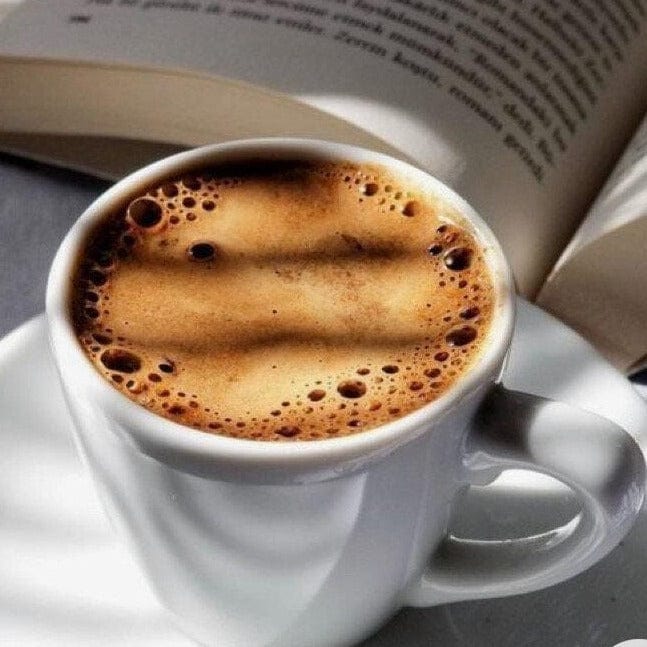 cup of black coffee on saucer with book open