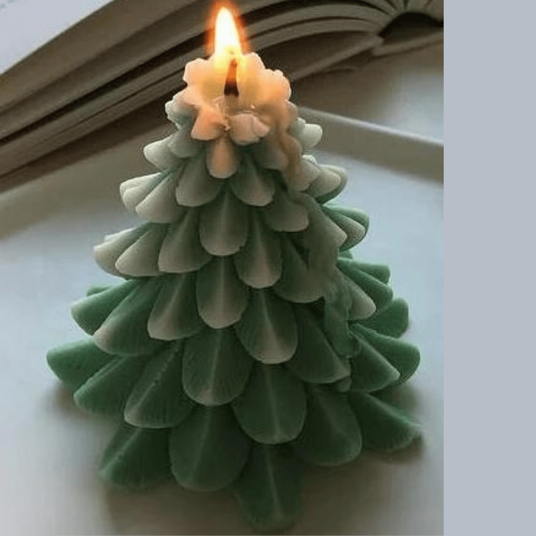 green flocked christmas tree candle with wick and flame on white table with book in background