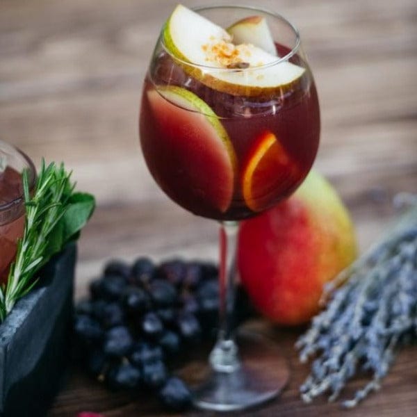 glass of grape punch with floating apples and fresh fruit surrounding