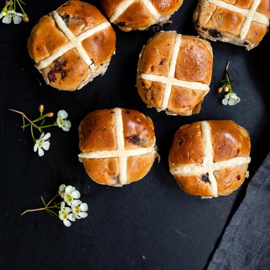 Fruit Hot Cross buns surrounded by florals on black tablecloth