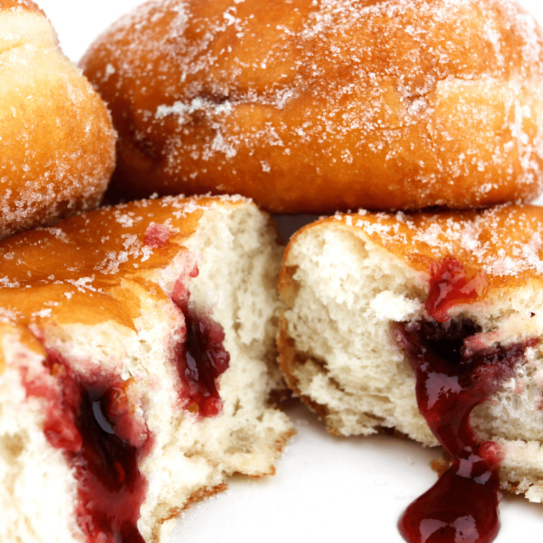 bunch of sugared donuts with raspberry jam oozing out