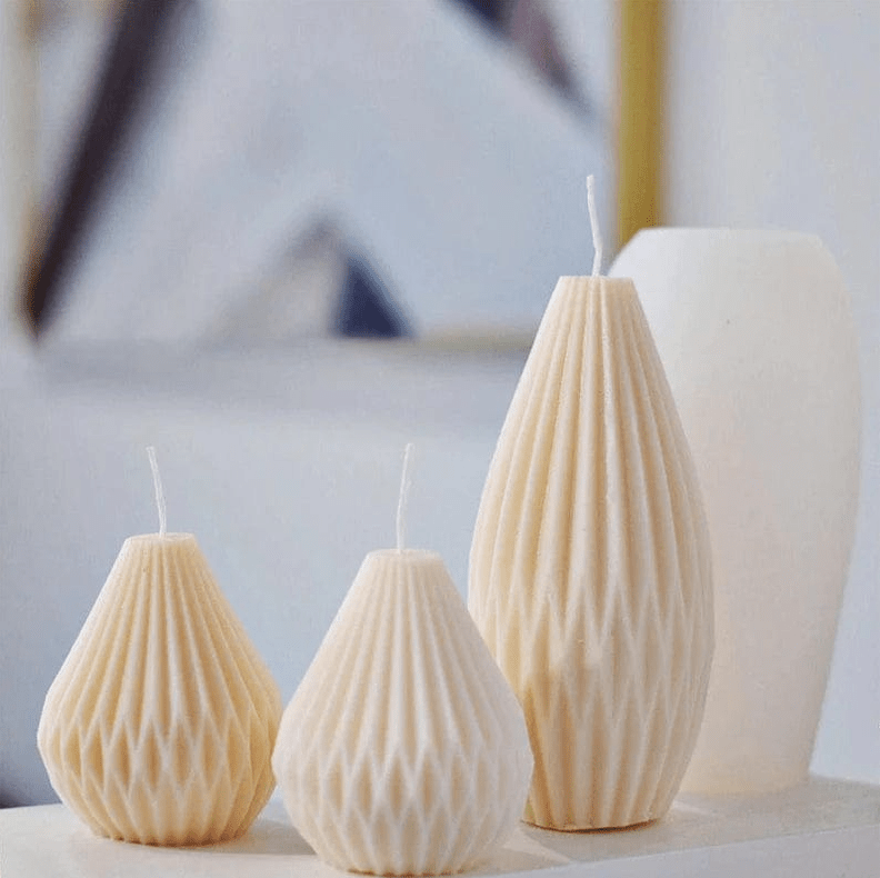 three lantern shaped candles in beige colours  in different sizes next to silicone mould with blurred background