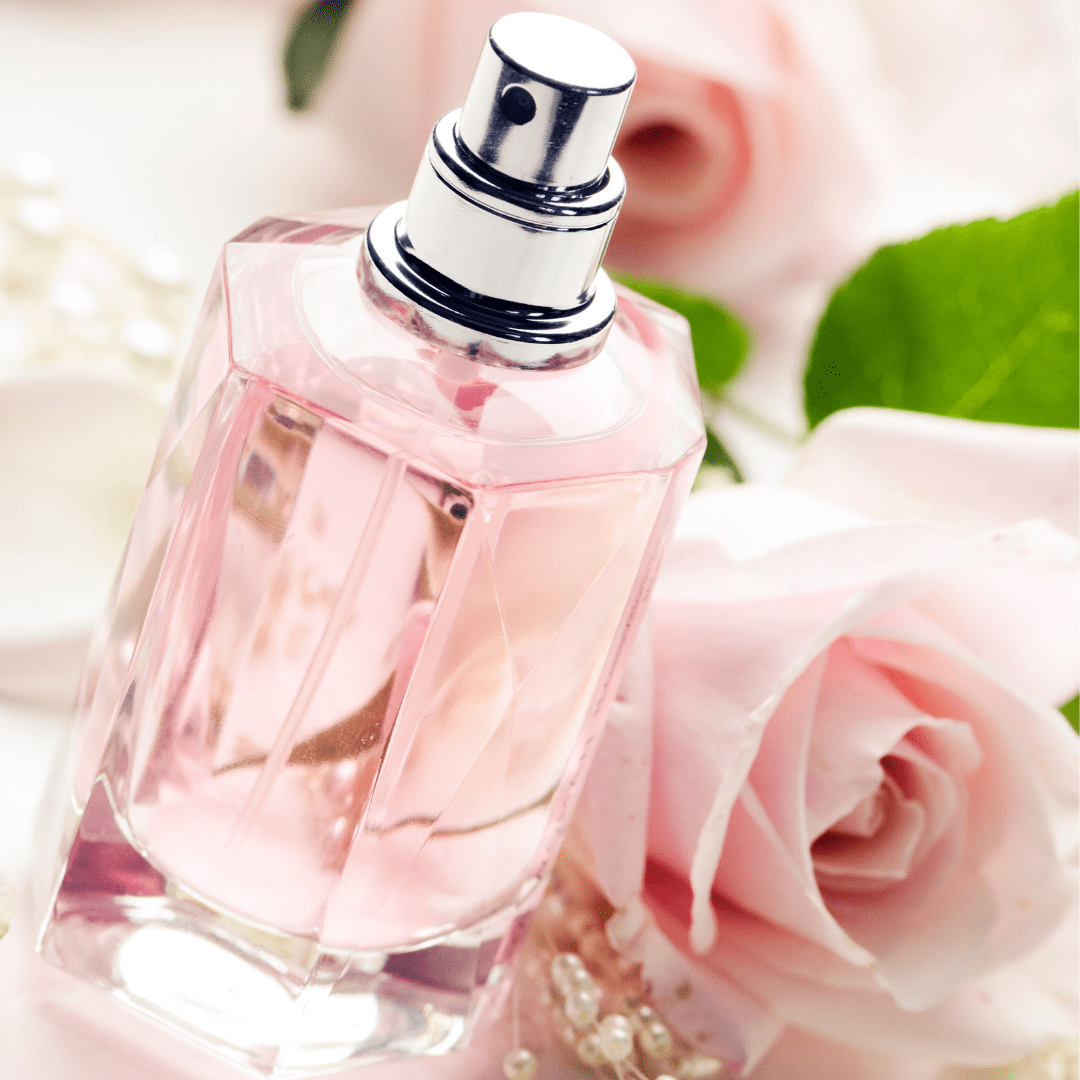 Perfume bottle filled with pink liquid and resting against pink roses