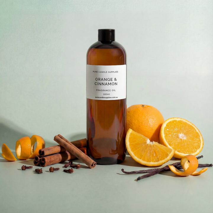 Bottle of 'Orange & Cinnamon' fragrance oil with oranges, cinnamon sticks, and vanilla beans on a light gray background