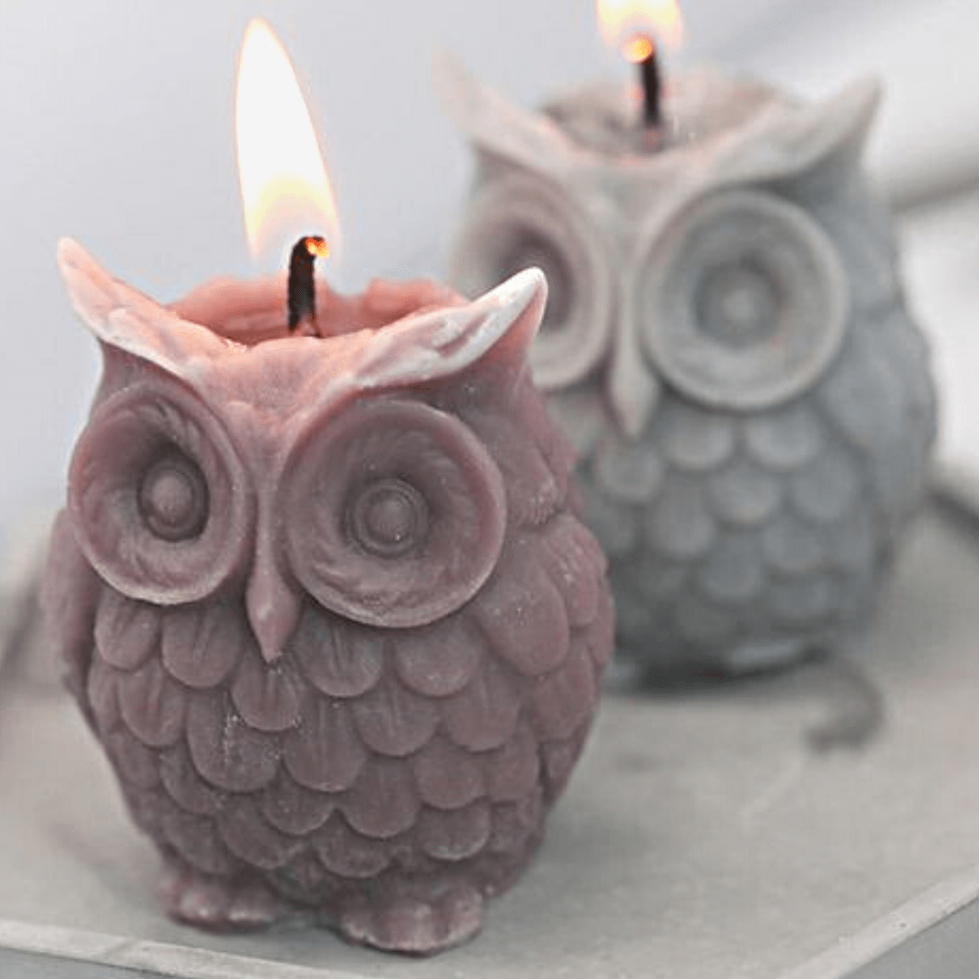 two owl shaped candles with flame in mauve and grey on a grey background