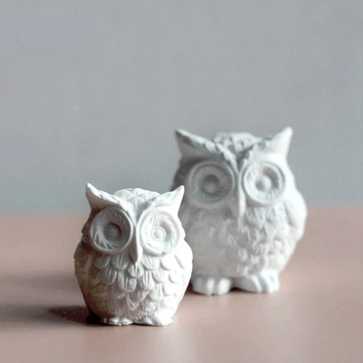 two owl shaped candles of different sizes on a brown and grey background