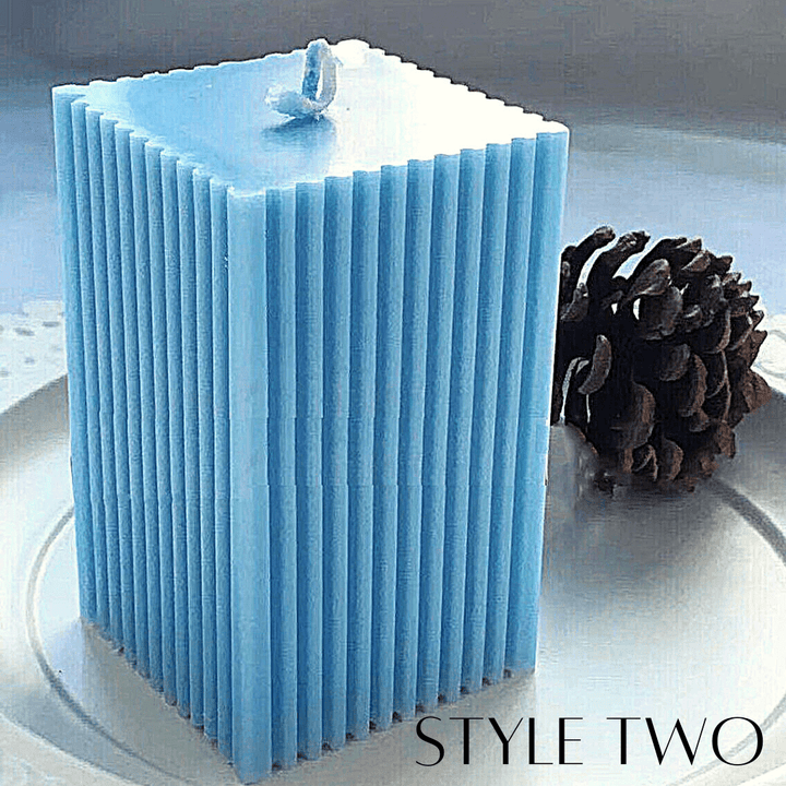 blue square pillar candle with ribbed edge design on a white stand with a pinecone in the background