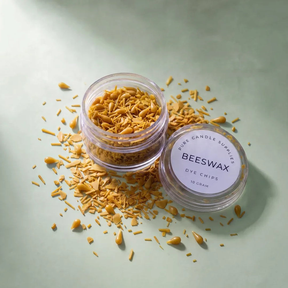 Pure Candle Supplies Melbourne beeswax dye chips in a small clear jar with scattered yellow wax pieces on a green surface