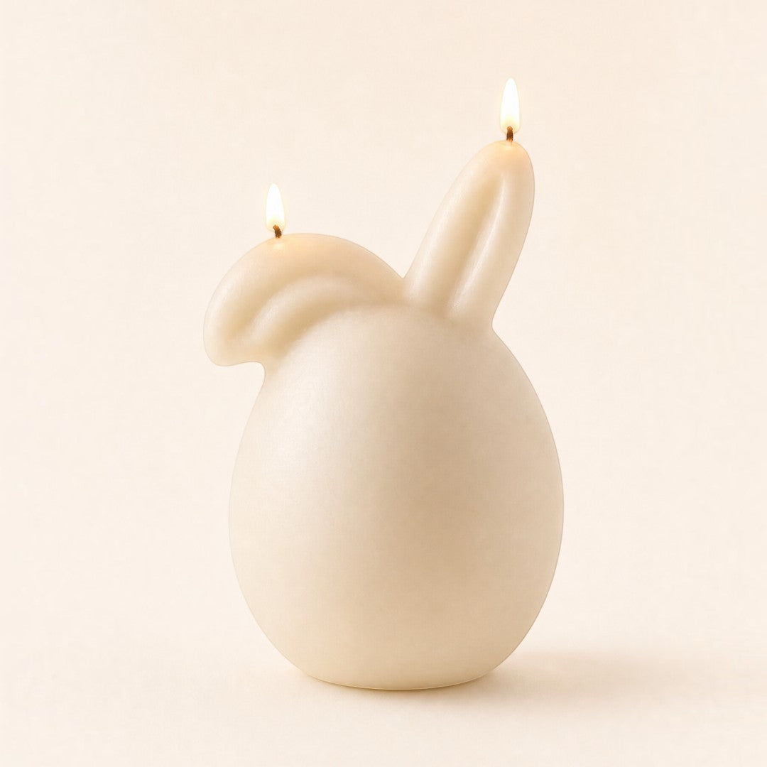 Pure Candle Supplies Melbourne bunny egg shaped candle with one ear down, lit and glowing against a neutral background.
