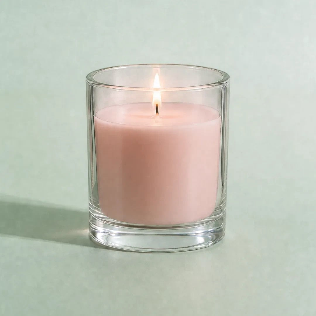 Pure Candle Supplies Melbourne dusty pink candle in a clear glass container with a lit wick on a soft green background