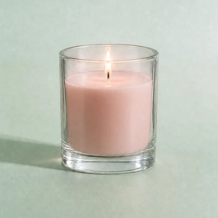Pure Candle Supplies Melbourne dusty pink candle in a clear glass container with a lit wick on a soft green background