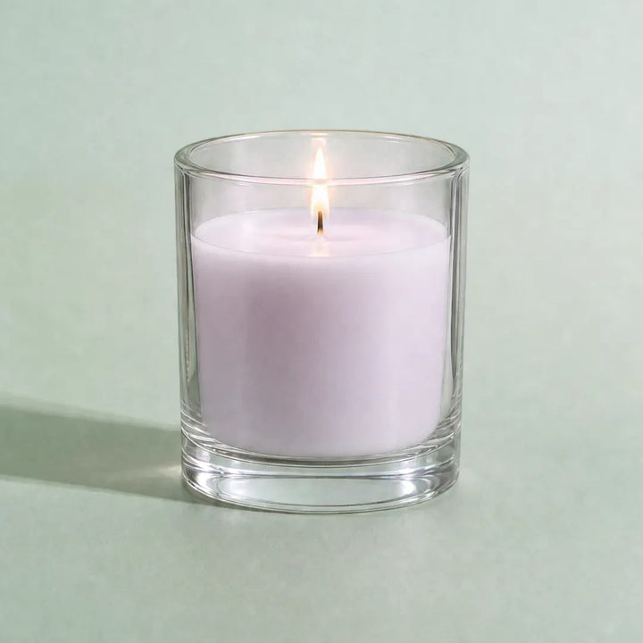 Pure Candle Supplies Melbourne lavender candle in a clear glass container with a lit wick on a soft green background