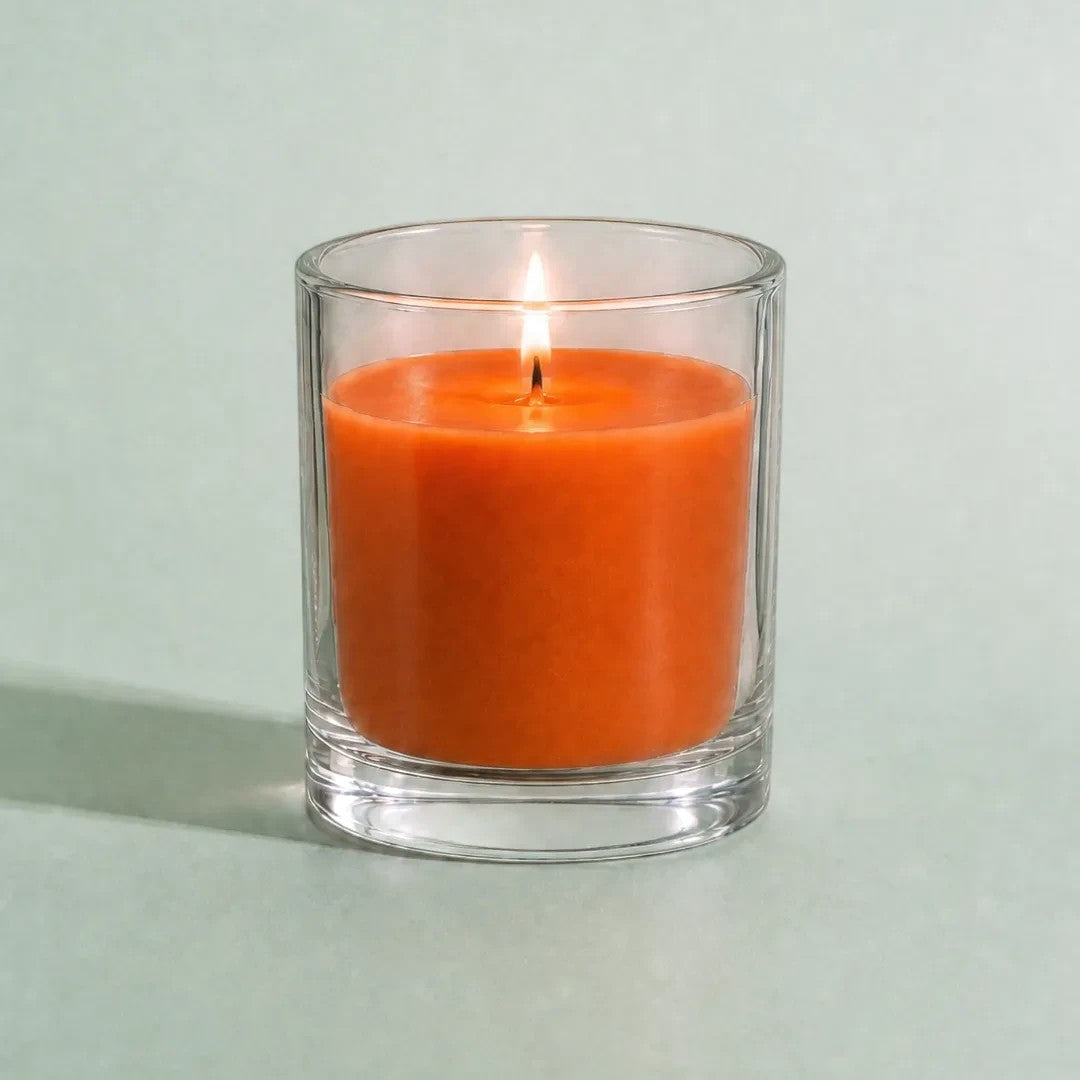 Pure Candle Supplies Melbourne rust orange candle in a clear glass container with a lit wick on a light green surface