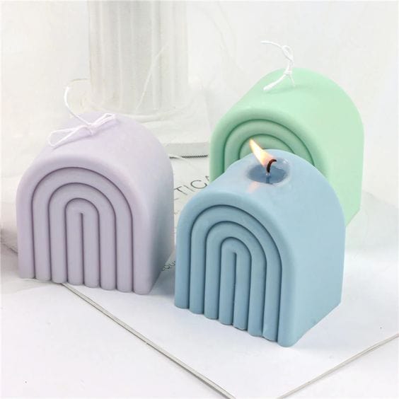 three wide rainbow shaped candles in blue purple and green on a white background