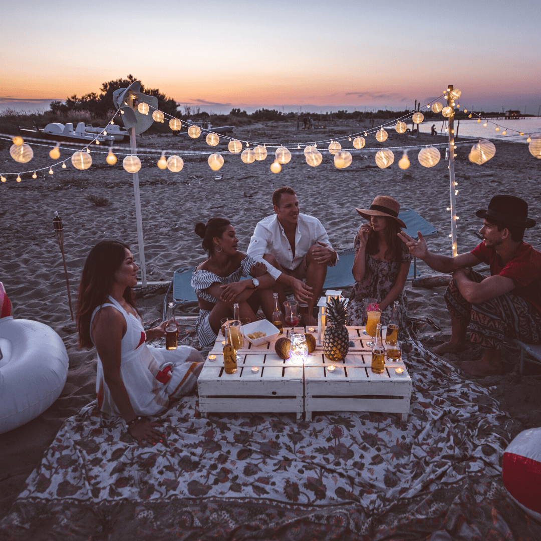 group of friends gathered on beach at sunset with drinks and fruits of pineapple & coconut