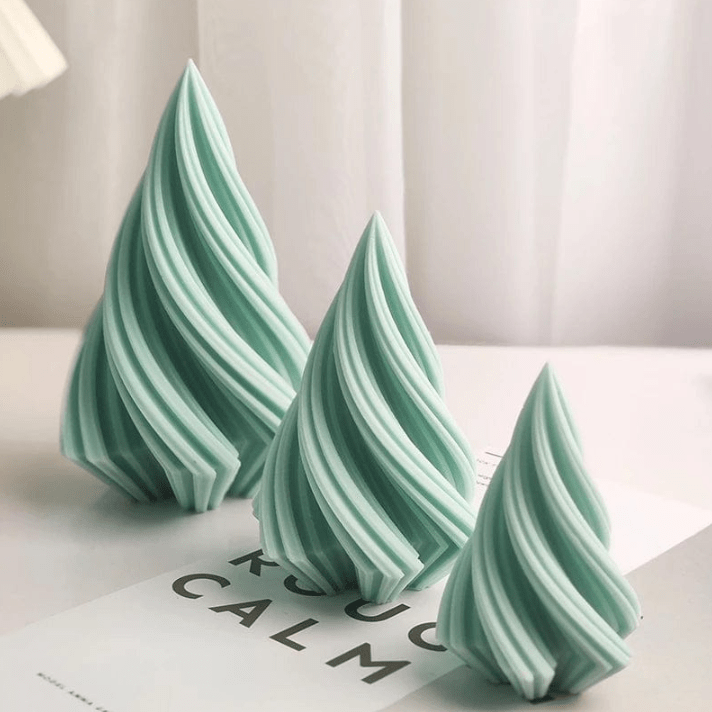 three spiral christmas trees of different size candles in green wax against white background
