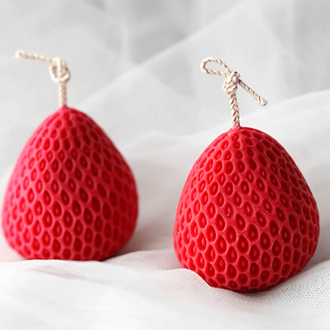 two strawberry shaped candle moulds in red wax against textured white background
