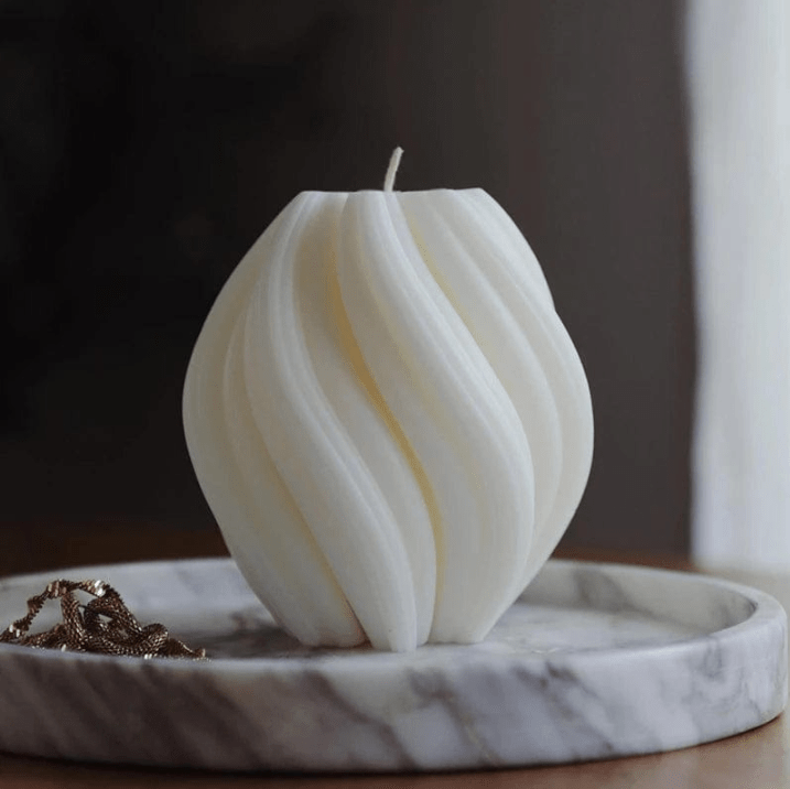large twist ball shaped candle in white wax on stone plate against blurred background