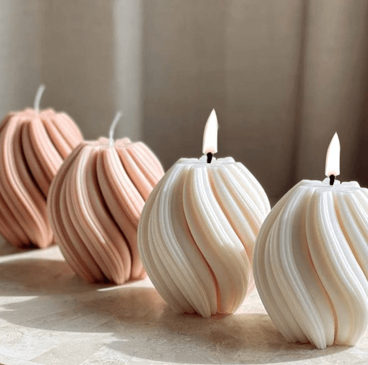 twist ball shaped candles in various shades of beige in a row  with 2 flames against beige background
