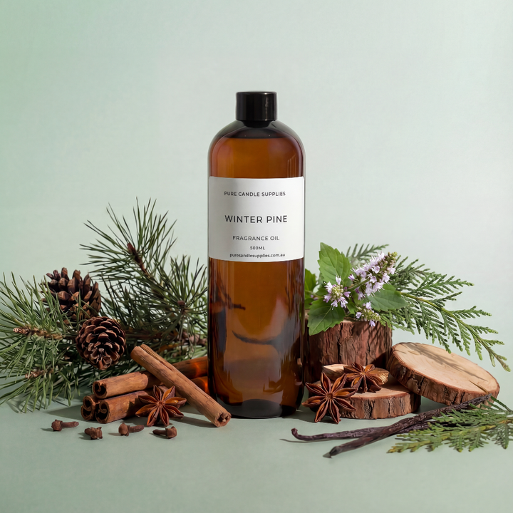 Bottle of 'Winter Pine' fragrance oil with pine branches, pinecones, and cinnamon sticks on a light green background